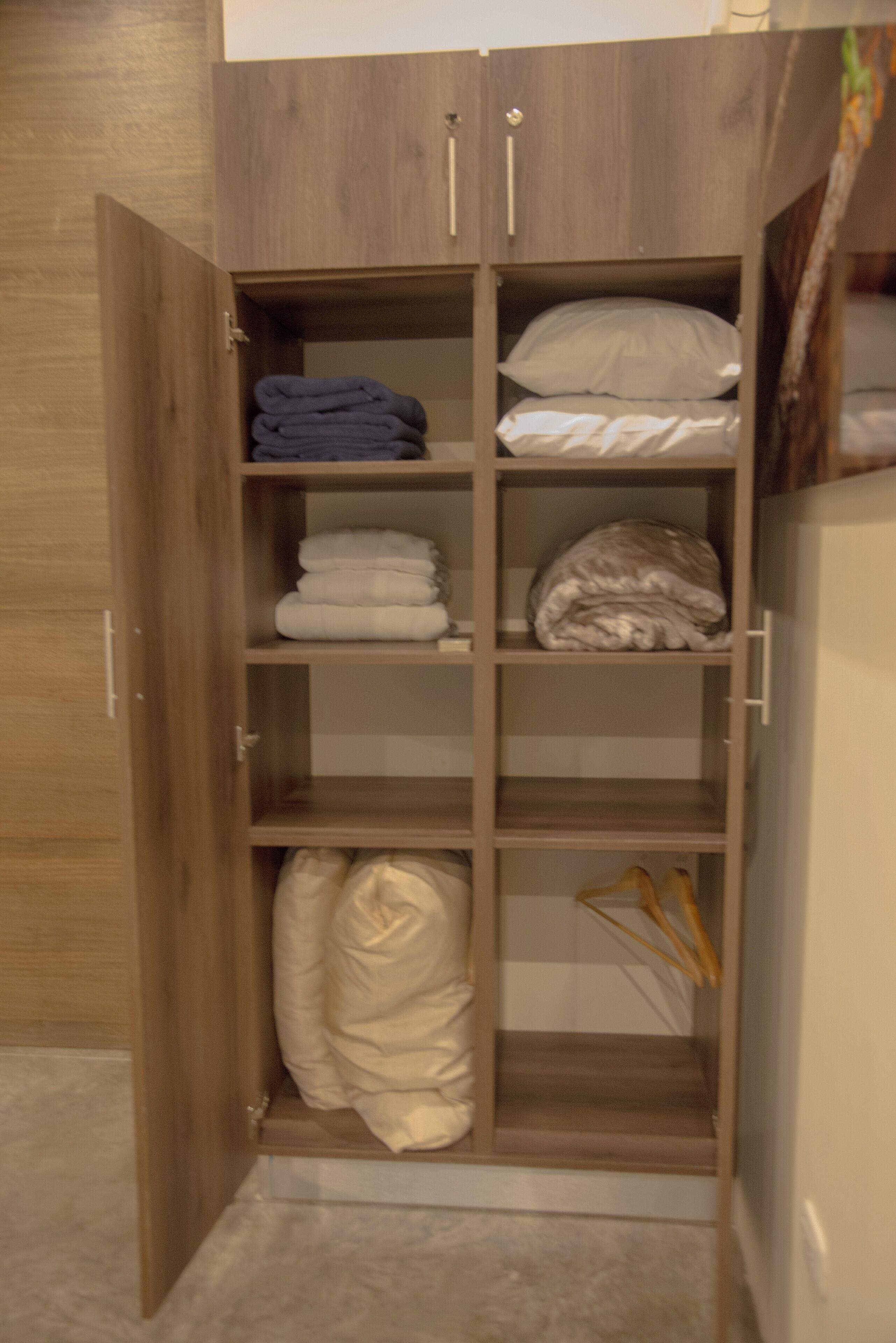 A wooden wardrobe with multiple shelves, some containing folded blankets and pillows.