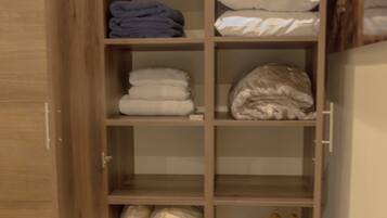 A wooden wardrobe with multiple shelves, some containing folded blankets and pillows.