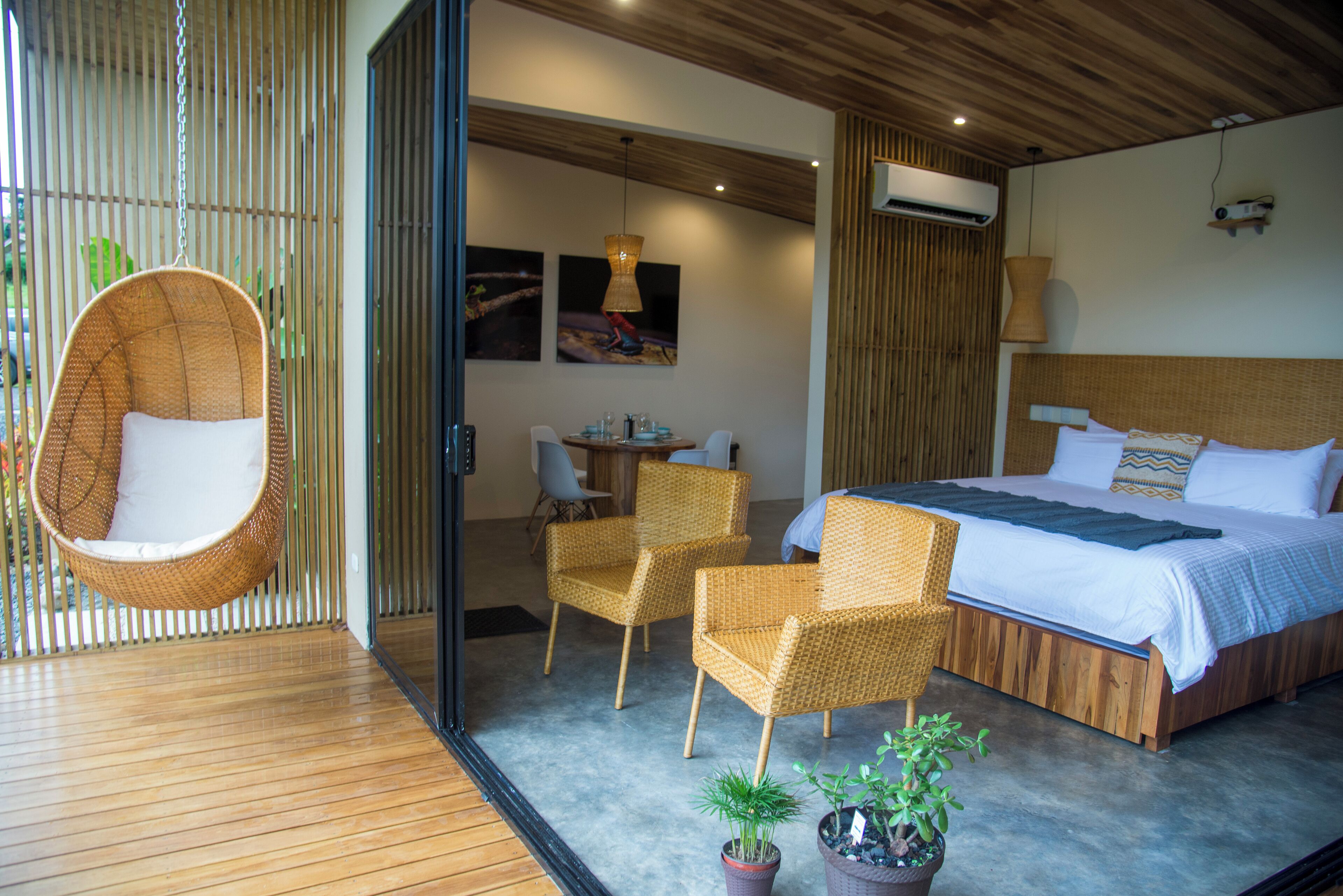 Een moderne slaapkamer met een groot bed, rieten stoelen, een hangstoel en een eethoek.