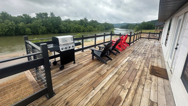 A wooden deck with a grill and red chairs overlooking a river.