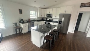 A modern kitchen with white cabinets, a granite countertop, stainless steel appliances, and a central island with bar stools.