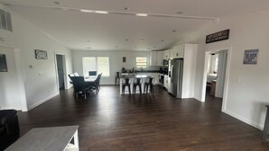 A spacious living area with a dining table and chairs, a kitchen with modern appliances, and a large window providing natural light.