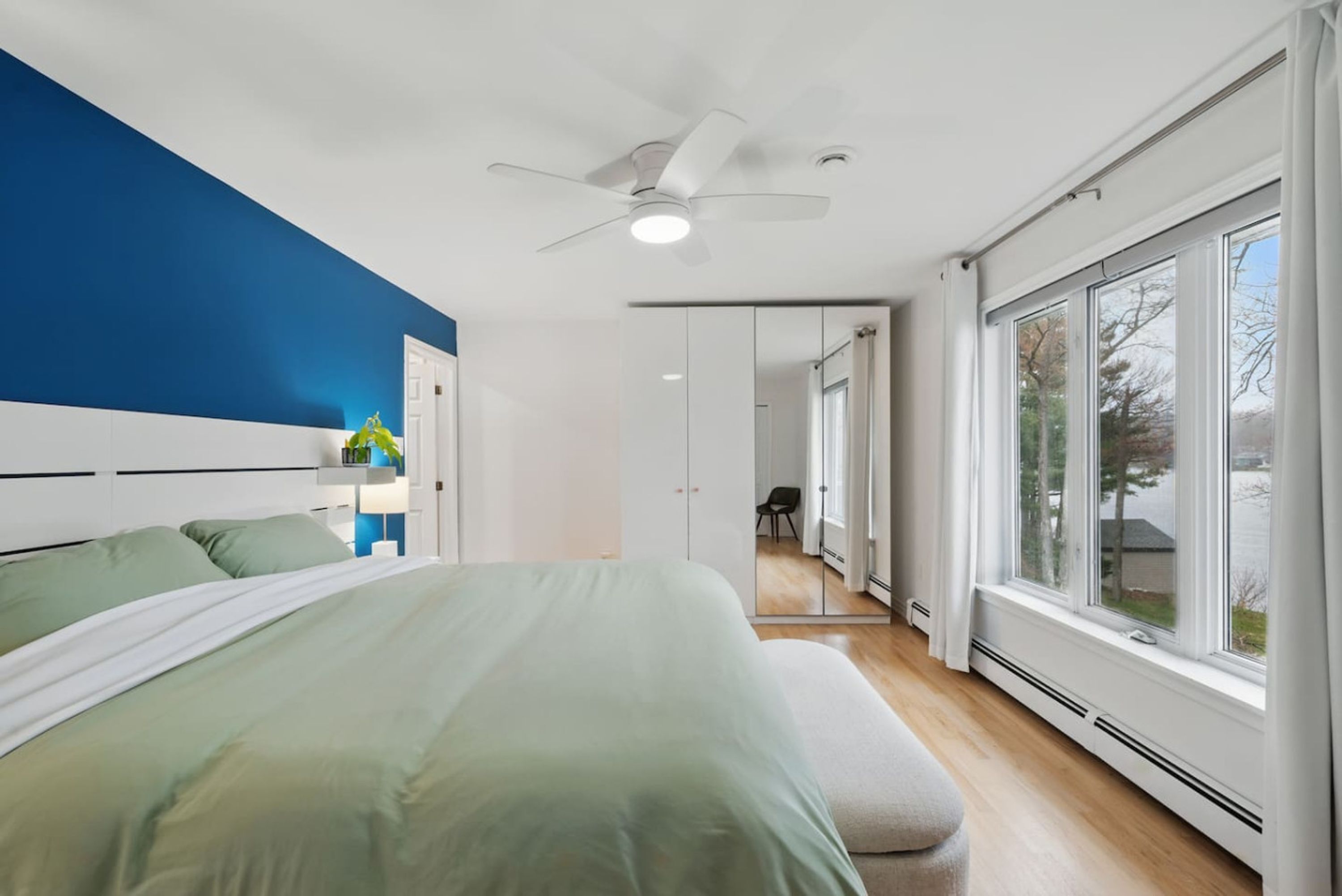 A modern bedroom with a bed, a ceiling fan, and large windows.