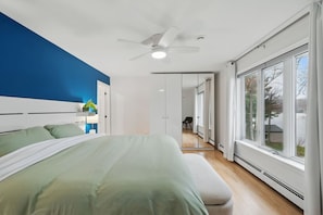 A modern bedroom with a bed, a ceiling fan, and large windows.