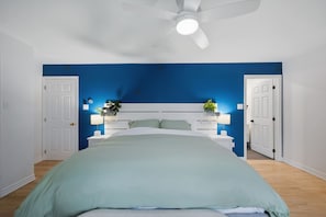 A bedroom with a bed, white headboard, two bedside tables with lamps, and a ceiling fan.