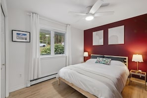 Quarto com cama, ventilador de teto, janela com cortinas e duas luminárias de cabeceira.