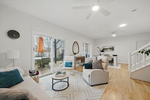 A spacious living room with a large window, a ceiling fan, and a staircase.