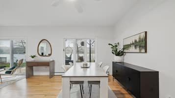 A modern living room with a dining table, chairs, a sofa, a TV cabinet, and a large window with a view of the outdoors.