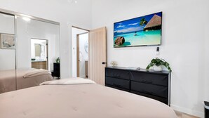 A bedroom with a large bed, a dresser, a TV on the wall, and a view of a beach scene. - Brand new Cottage, putting green, private patio (Thousand Oaks)