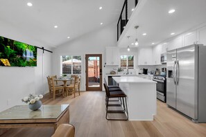 A modern kitchen with a central island, stainless steel appliances, and a dining area with a table and chairs. - Brand new Cottage, putting green, private patio (Thousand Oaks)