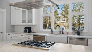 A modern kitchen with a gas stove, white cabinets, a built-in oven, and a window with a view of trees.