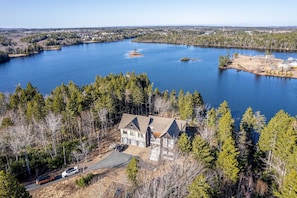 A large house with a garage and driveway, surrounded by dense forest and a lake. - Private Lakefront Mansion on Schmidt Lake (Hammonds Plains)