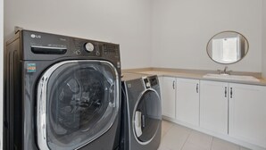 A laundry room with two LG washing machines, a sink, and a mirror.