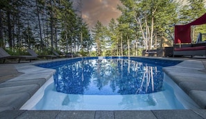 A rectangular swimming pool with clear blue water, surrounded by a stone deck and wooden lounge chairs. - Private Lakefront Mansion on Schmidt Lake (Hammonds Plains)