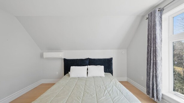 A bedroom with a bed, white walls, a sloped ceiling, and a window with curtains.