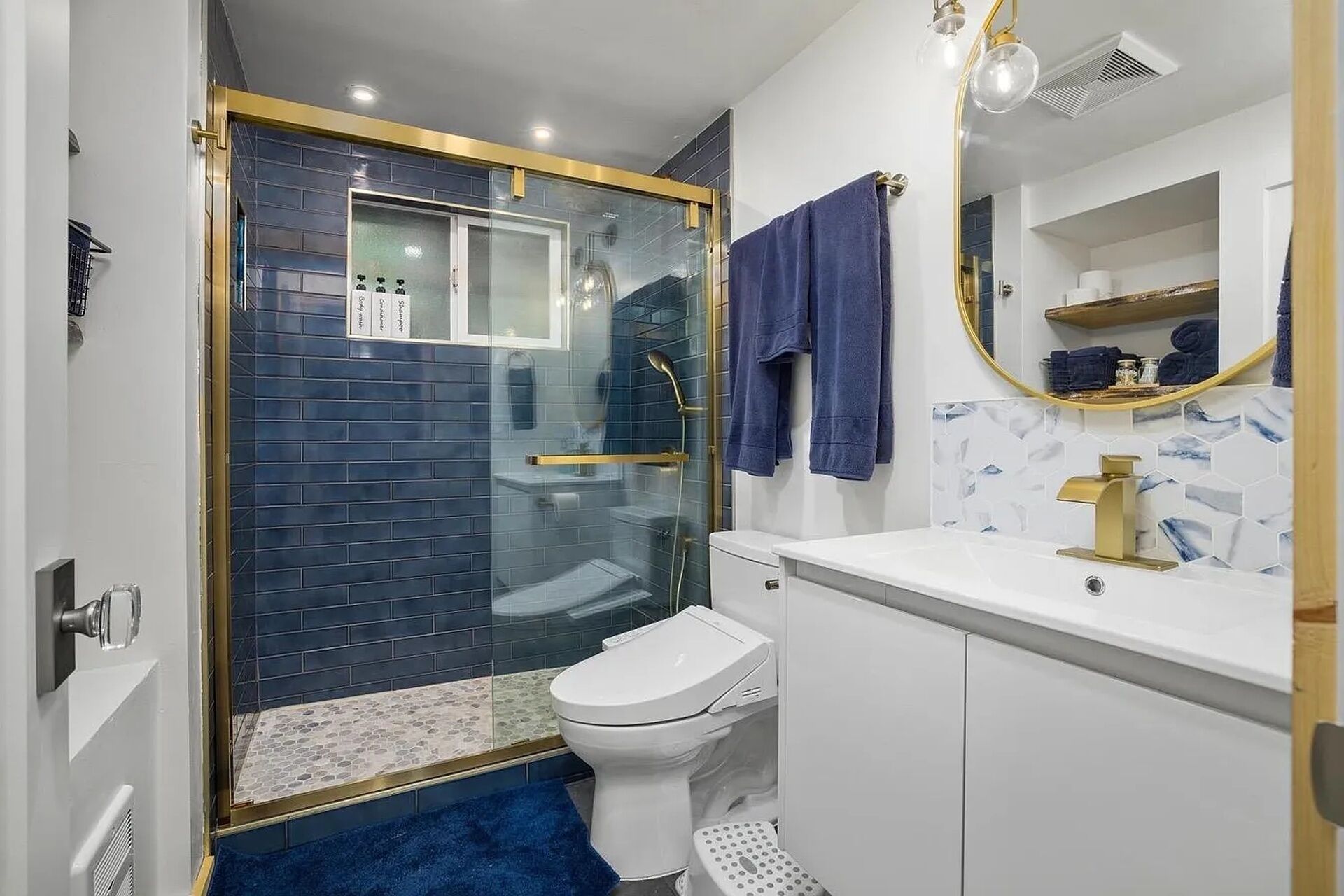 Ein Badezimmer mit einer Duschkabine, einer weißen Toilette und einem weißen Waschbecken mit goldfarbenem Wasserhahn.