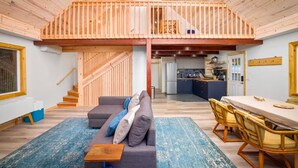 A spacious loft-style living area with a high ceiling, a staircase leading to an upper level, a kitchen, and a dining area.