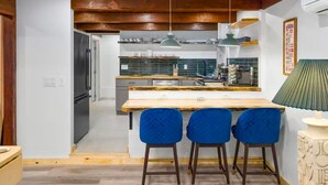 A modern kitchen with a wooden island, bar stools, pendant lights, and a green lamp.