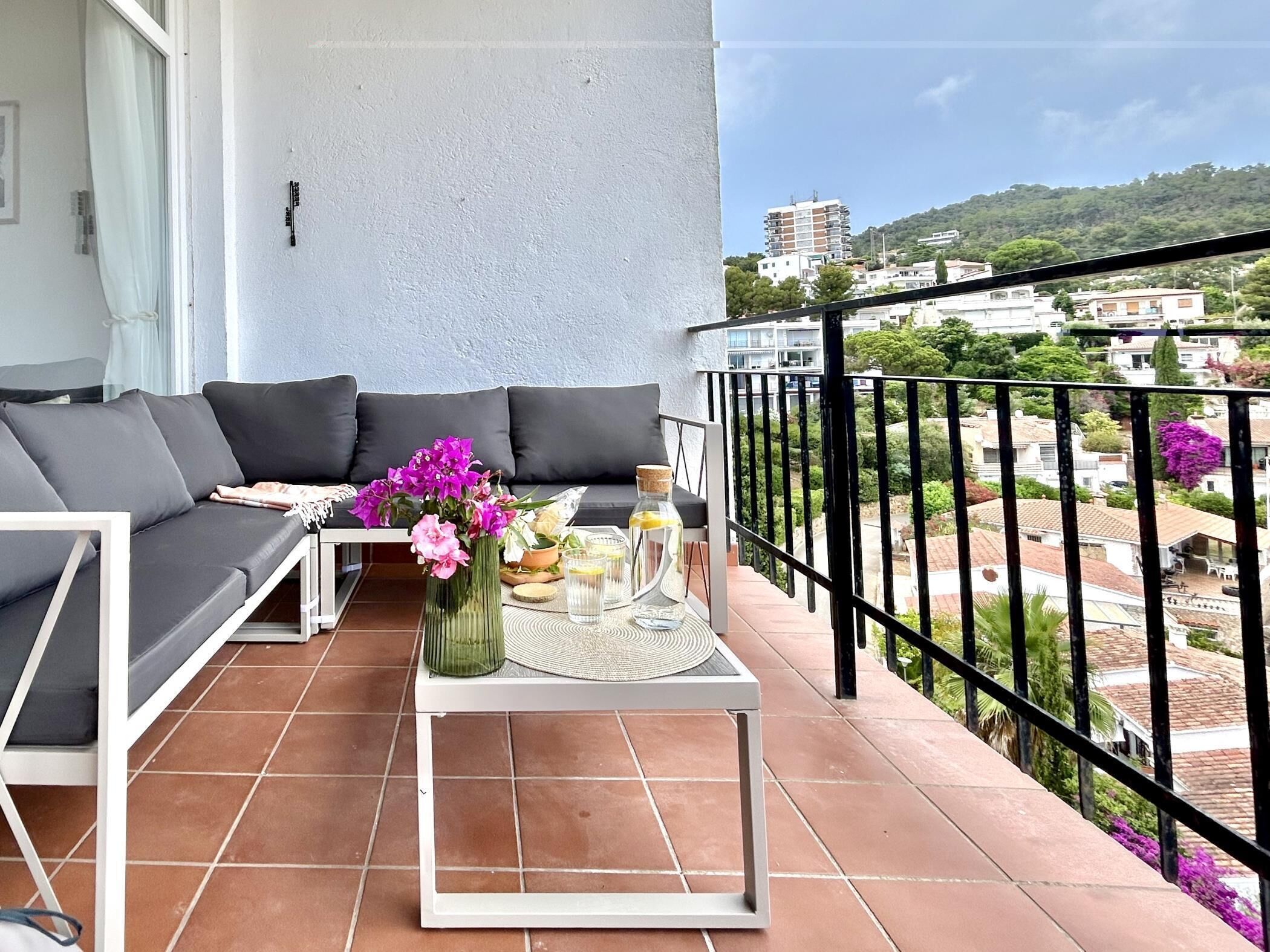 A balcony with a sofa, a small table, and a view of the cityscape.