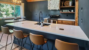 Une cuisine moderne dotée d’un grand îlot central, de tabourets de bar, d’un mur décoratif en pierre et d’un luminaire suspendu.