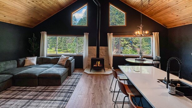 Une pièce confortable de style loft, dotée d’un haut plafond, d’une cheminée, d’un coin repas et de grandes fenêtres offrant une vue sur l’extérieur.