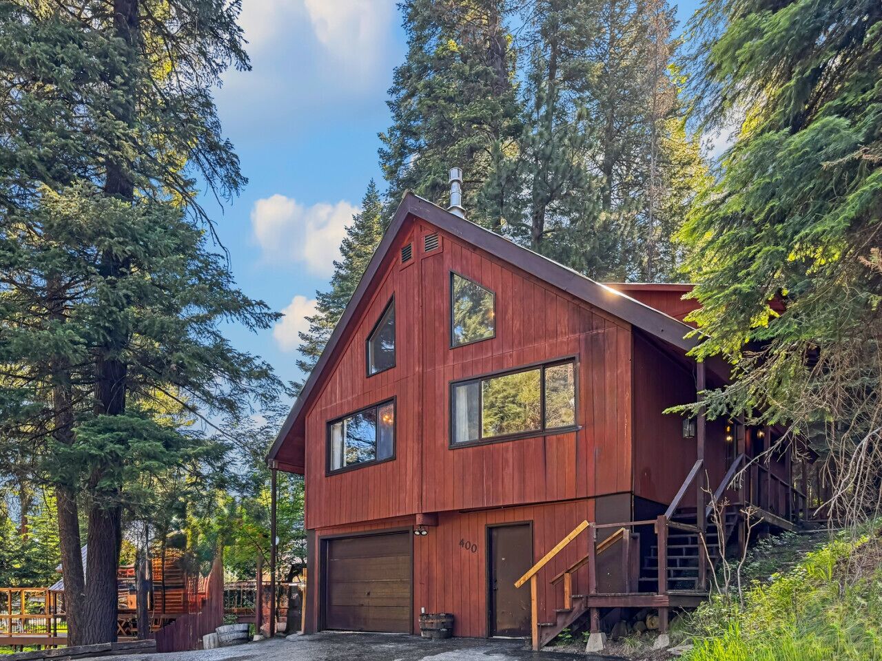 A two-story wooden cabin with a garage, surrounded by tall trees.