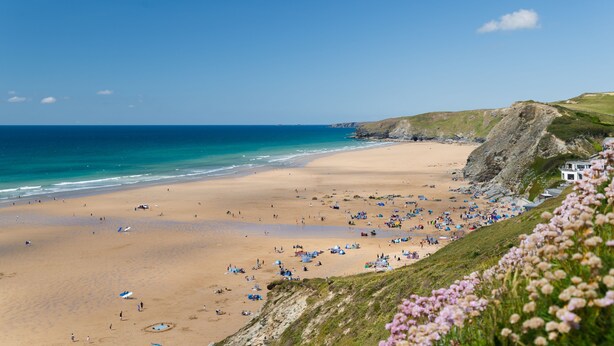 A beach with people and umbrellas, a building on the right, and a cliff. - 26 Waves - sleeps 4 guests  in 1 bedroom (Watergate Bay)