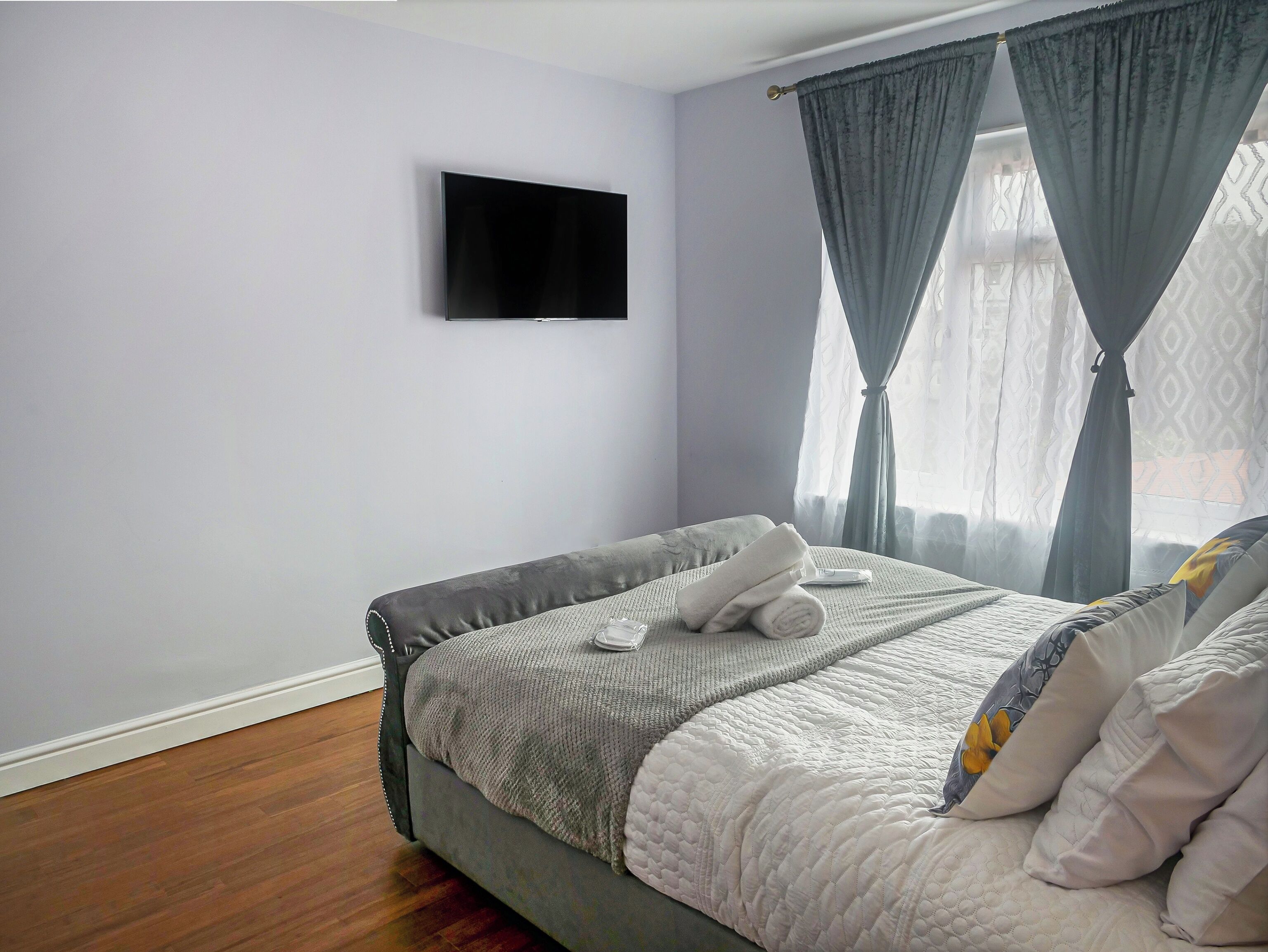 A bedroom with a bed, a flat-screen TV, and a window with curtains.