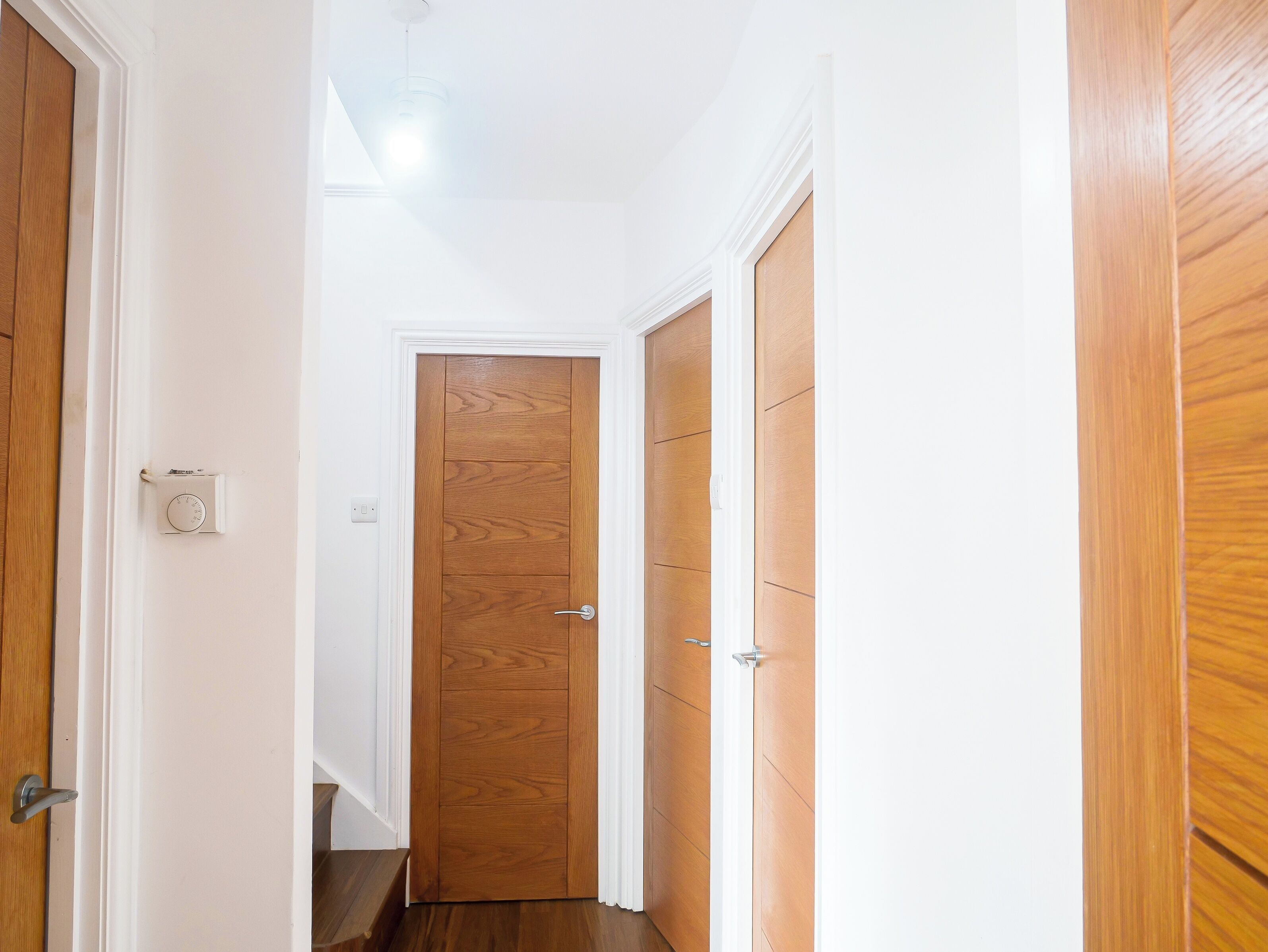 Un pasillo estrecho con puertas de madera y un termostato en la pared.