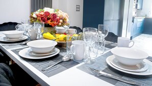 Ein moderner Essbereich mit einem Tisch, der für vier Personen gedeckt ist, einschließlich Tellern, Schüsseln, Gläsern und Besteck. Auf dem Tisch steht eine Vase mit Blumen, und der Raum hat ein zeitgemäßes Design mit blauen Schränken und einer neutralen Farbpalette.