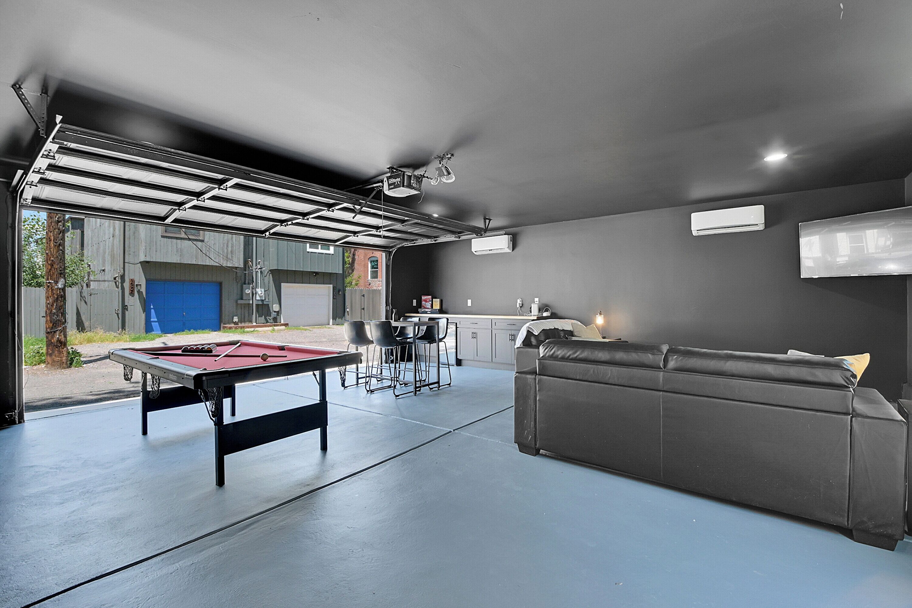 A garage with a pool table, a sofa, and a dining area.