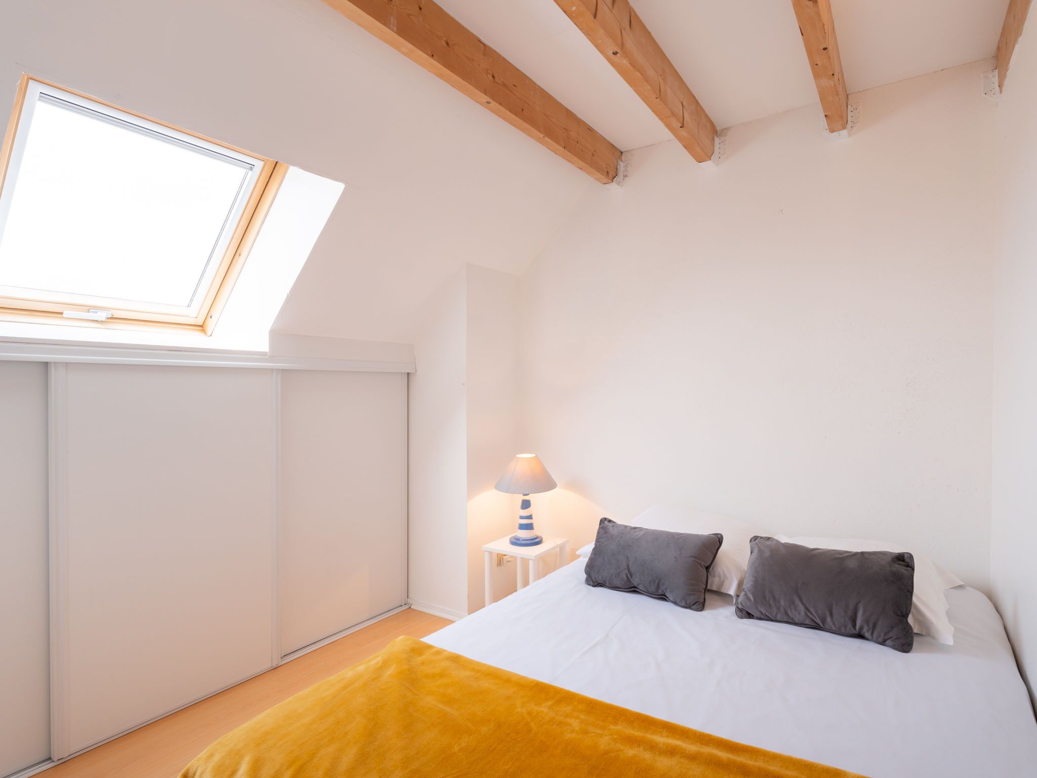 A bedroom with a skylight, a bed with two pillows, a bedside lamp, and a yellow throw blanket.