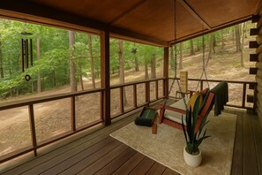 Una terraza de madera con una silla mecedora, un banco y una planta en maceta.