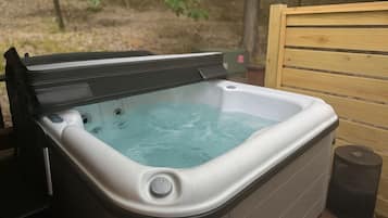A hot tub with a wooden deck and a trash can nearby.