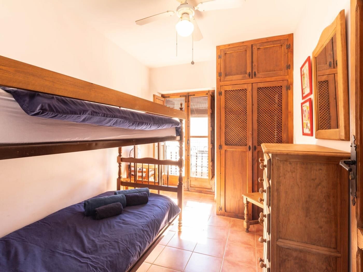 A bunk bed with a blue mattress and pillows, wooden wardrobe, and a ceiling fan.