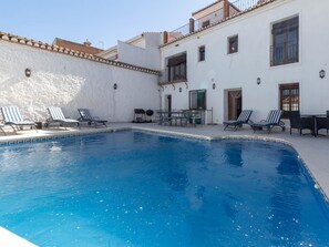 A swimming pool with lounge chairs and a table, surrounded by a white building with balconies. - Beautiful rural house with swimming pool and barbecue (Cozvíjar)