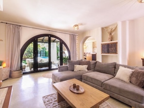 A living room with a sofa, a wooden coffee table, and a view of a pool through an arched doorway.