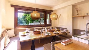 A dining area with a large window, a wooden table set for a meal, and a built-in bench. - Beautiful house with pool in the heart of the Lecrín Valley (Restábal)