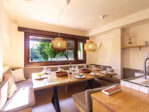 A dining area with a wooden table set for four, a bench seating, and a window with a view of greenery.