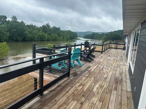 Een houten terras met stoelen en een barbecue, met uitzicht op een rivier en beboste heuvels.