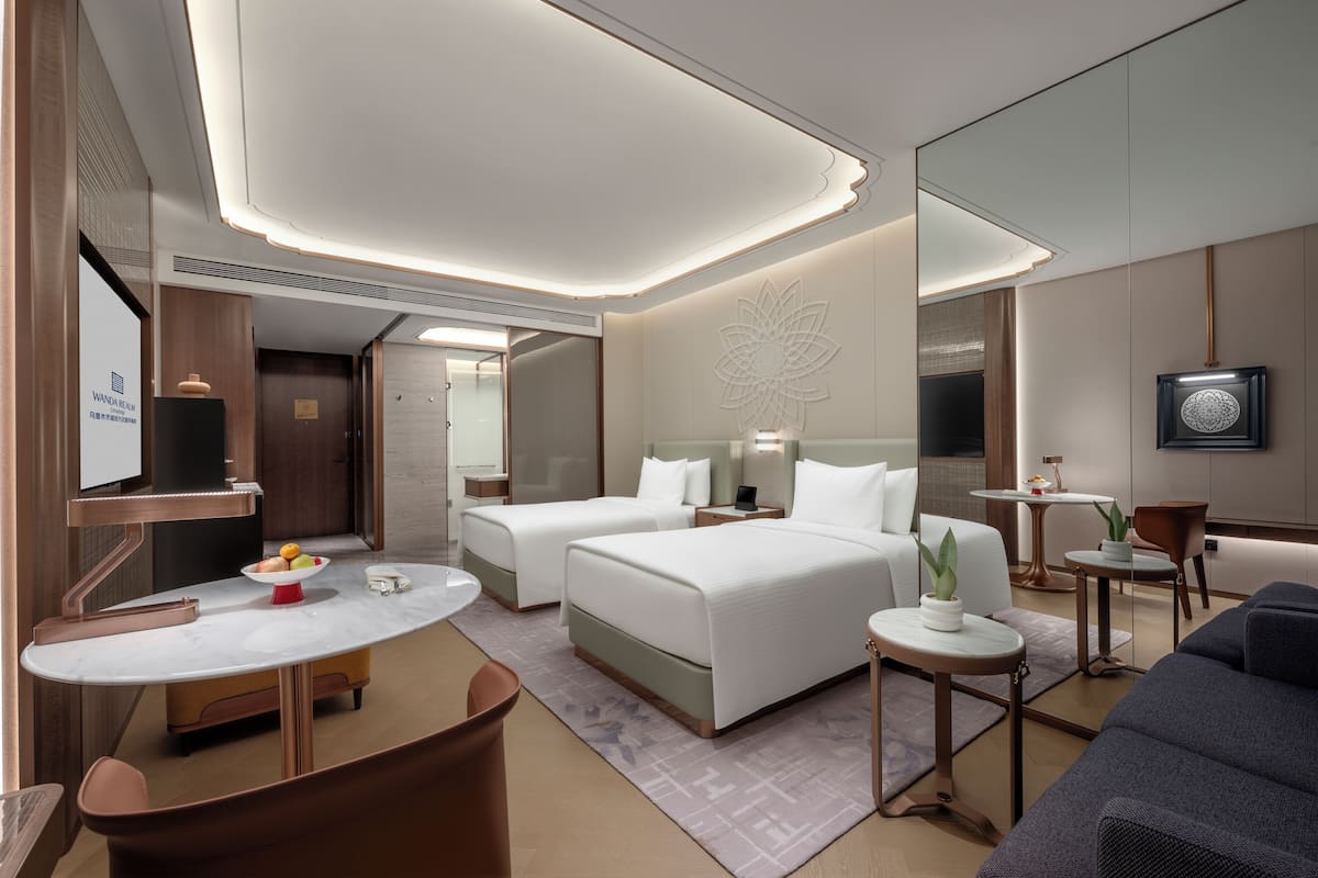 A modern hotel room with two beds, a dining area, a sitting area, and a TV.