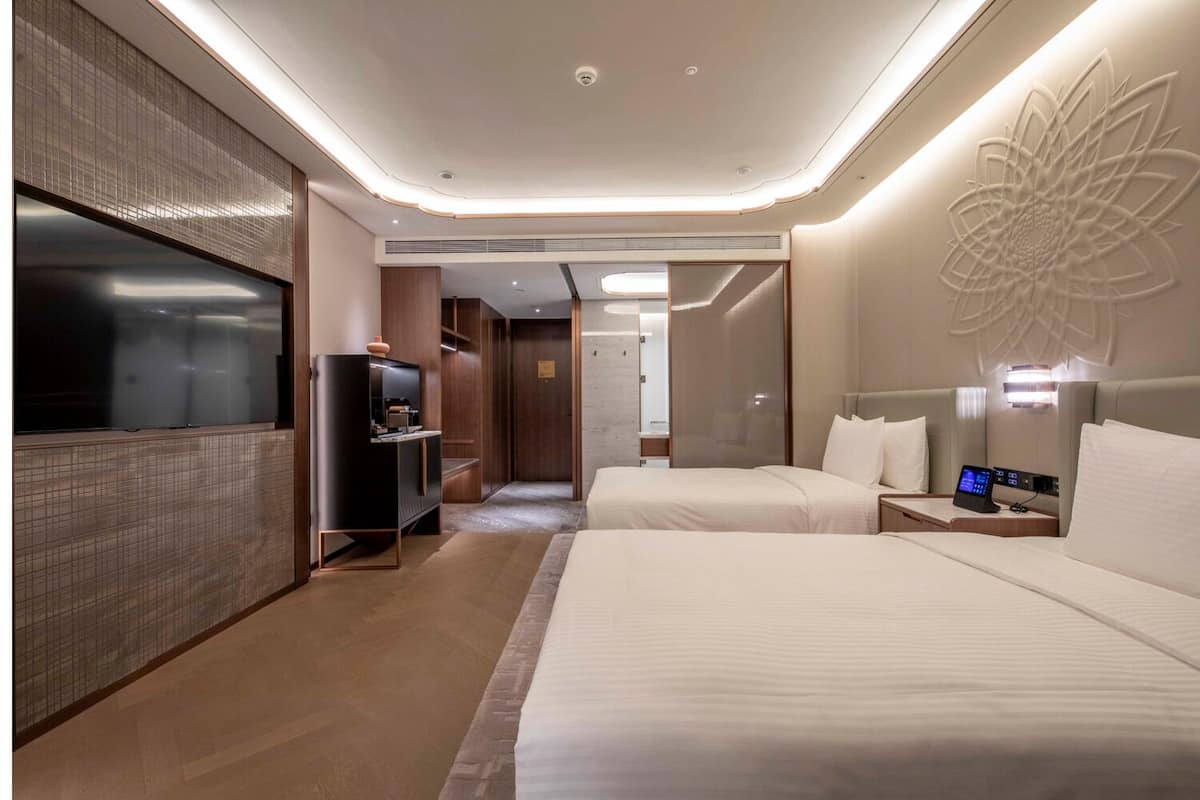 A modern hotel room with a large bed, a TV, and a desk with a control panel.