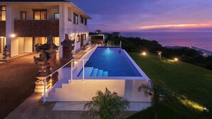 Une maison moderne dotée d’une piscine, d’un patio bien éclairé et offrant une vue sur l’océan au crépuscule.