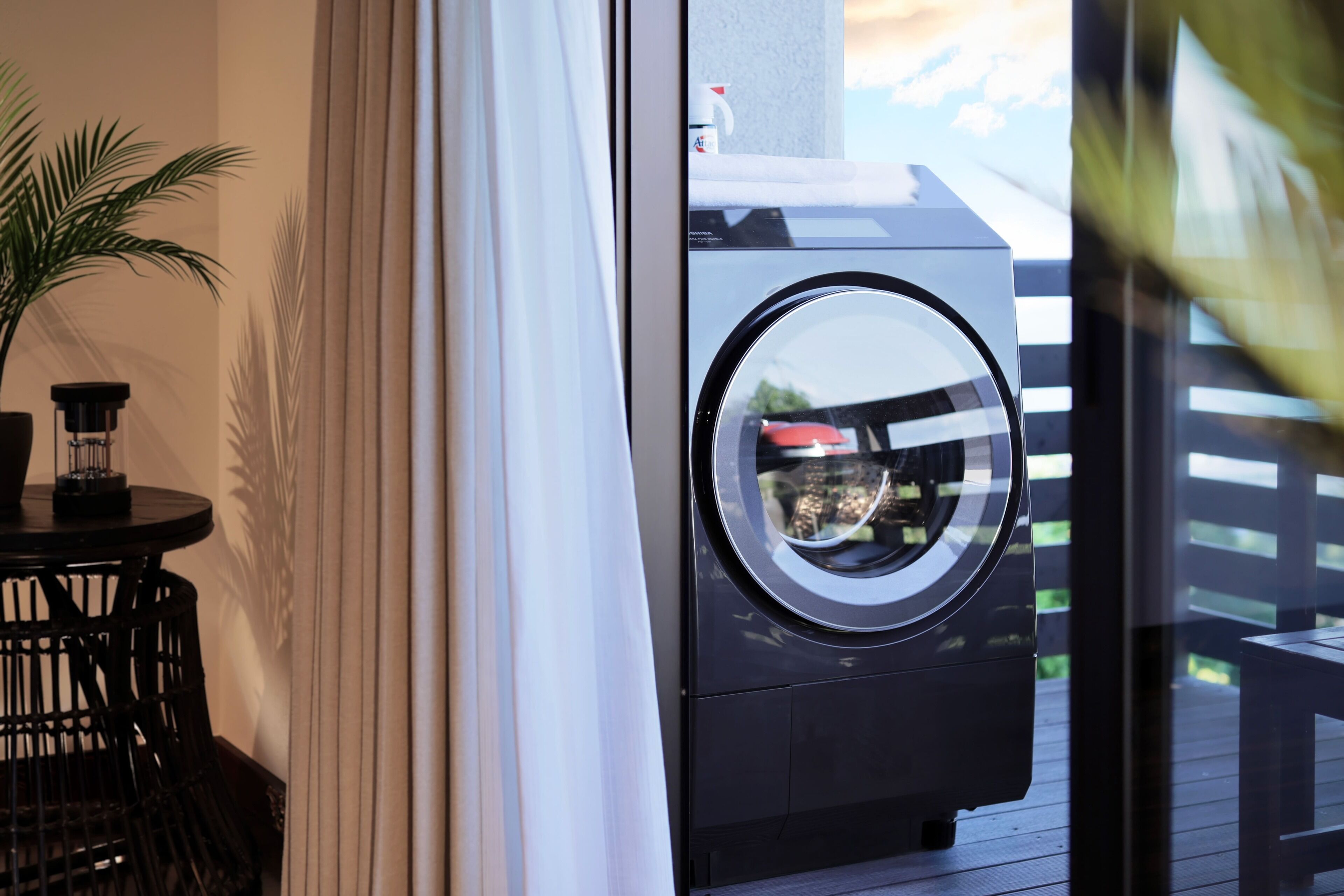 Un lave-linge et un sèche-linge à chargement frontal, installés sur un balcon, avec une plante en pot et une petite table.