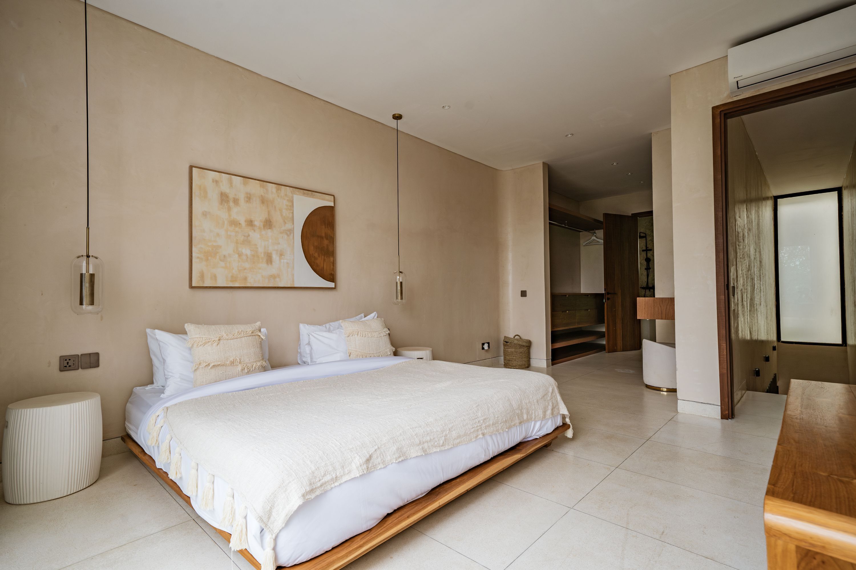 A spacious bedroom with a large bed, a bedside table, a wall-mounted artwork, and a view into the adjacent bathroom.