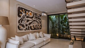 Een moderne woonkamer met een witte bank, een groot abstract schilderij en een glazen deur die uitkomt op een groen buitengebied.