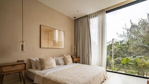 Een slaapkamer met een groot bed, een houten nachtkastje, een wandlamp en uitzicht op groen door een raam.