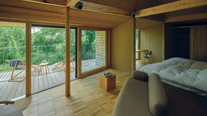 Un dormitorio con una cama grande, piso de madera, balcón con mesa y sillas, y ventilador de techo.