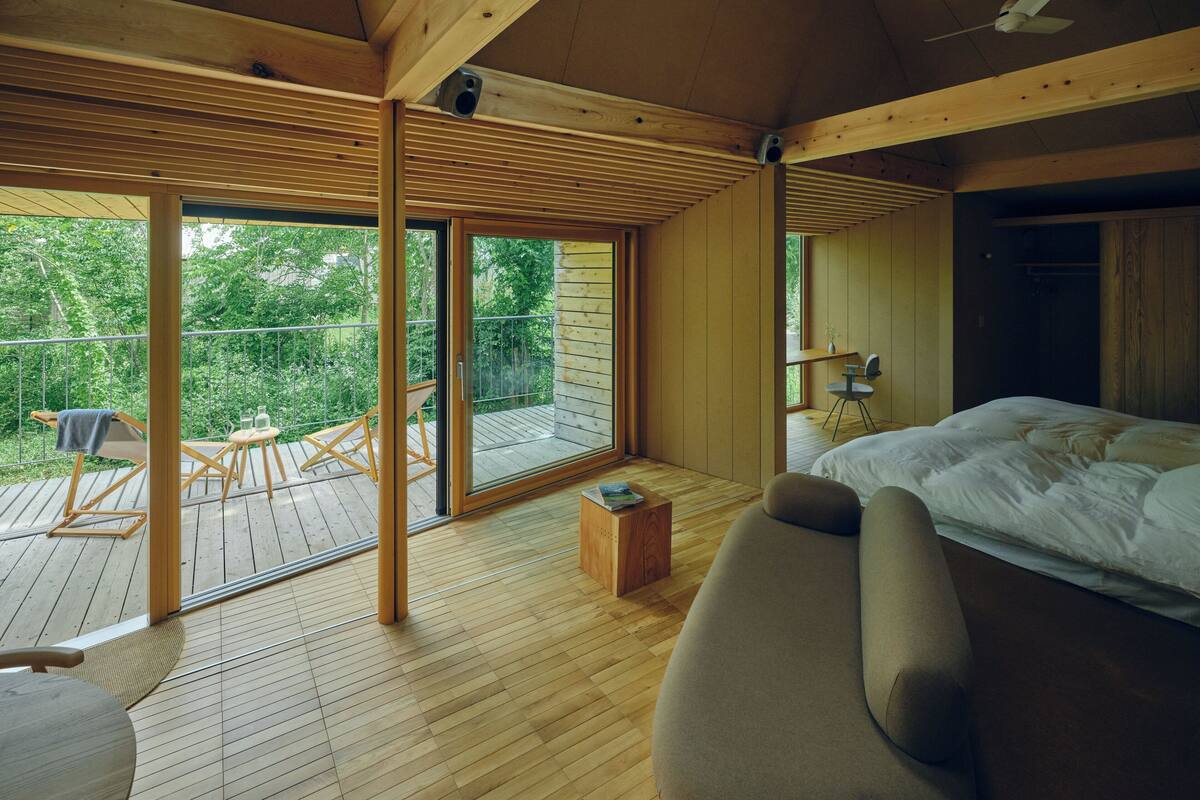 Une chambre avec un grand lit, un plancher en bois, un balcon avec une table et des chaises, et un ventilateur de plafond.
