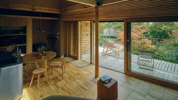 A modern wooden interior with a dining area, kitchen, and large sliding glass doors leading to an outdoor deck.